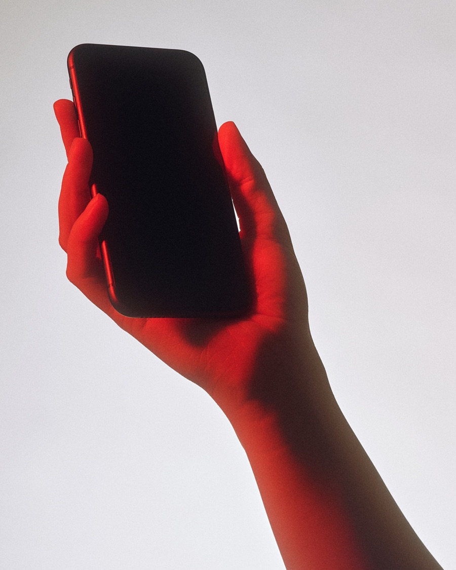 A hand lit in red holding up a phone